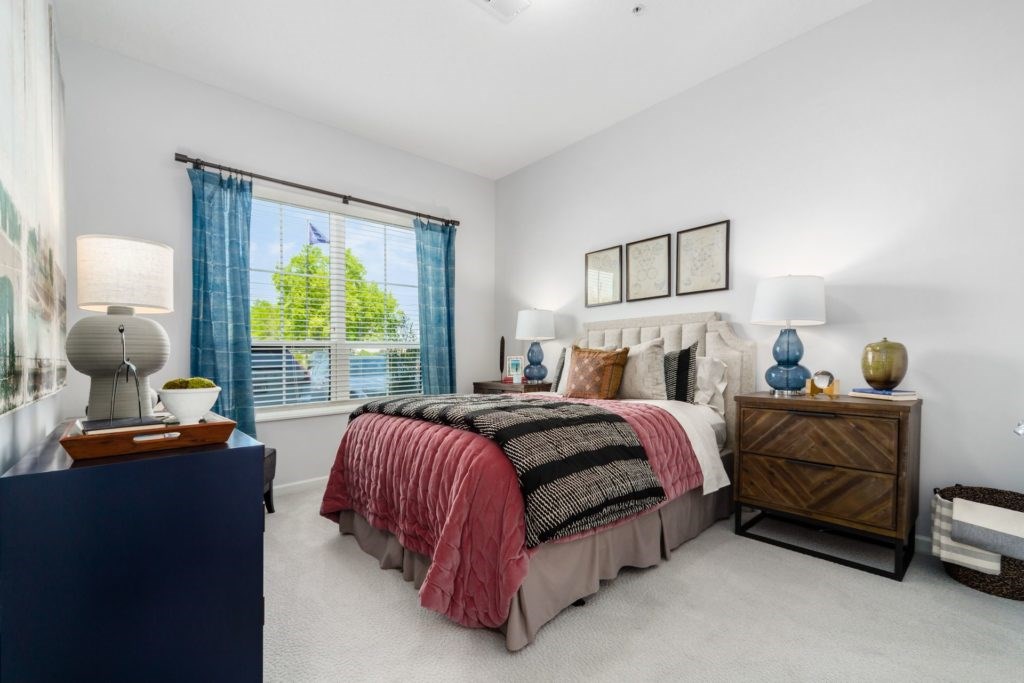 A bedroom with a bed, nightstand, and window with blue curtains.