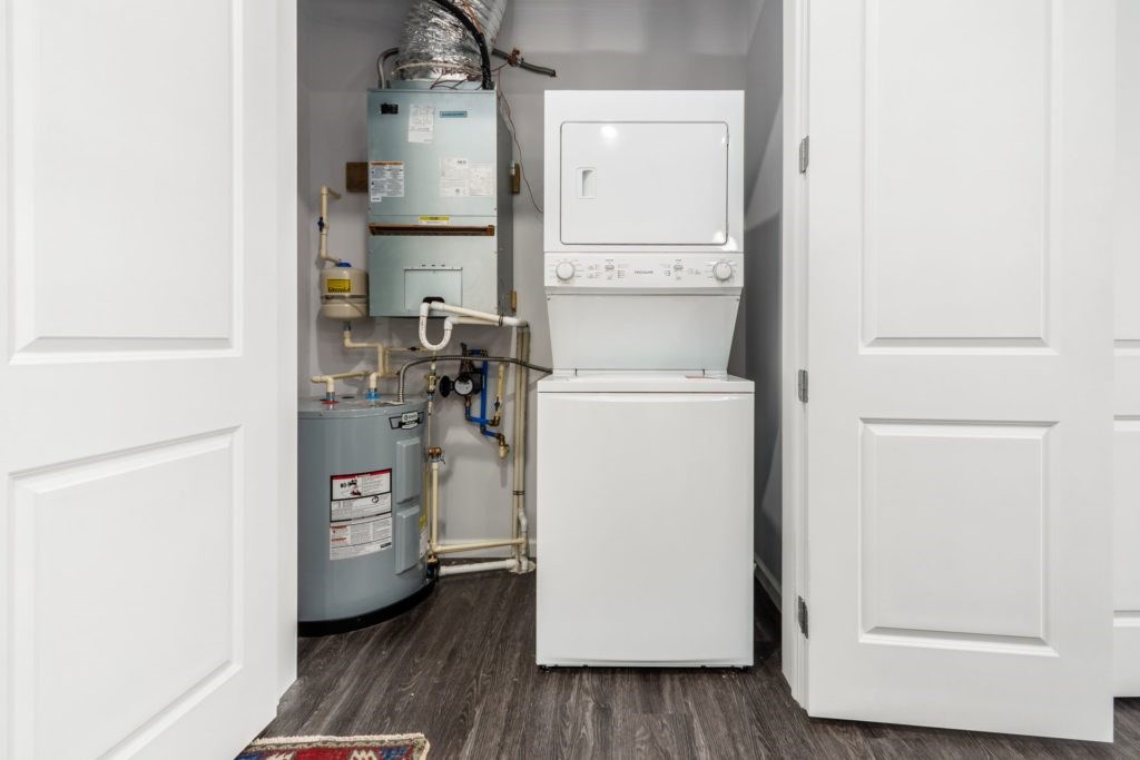 A white tankless water heater sits in a narrow space between two doors.