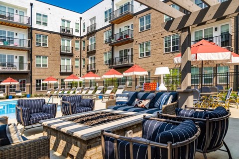 A poolside area with lounge chairs and umbrellas in front of a multi-story apartment building.
