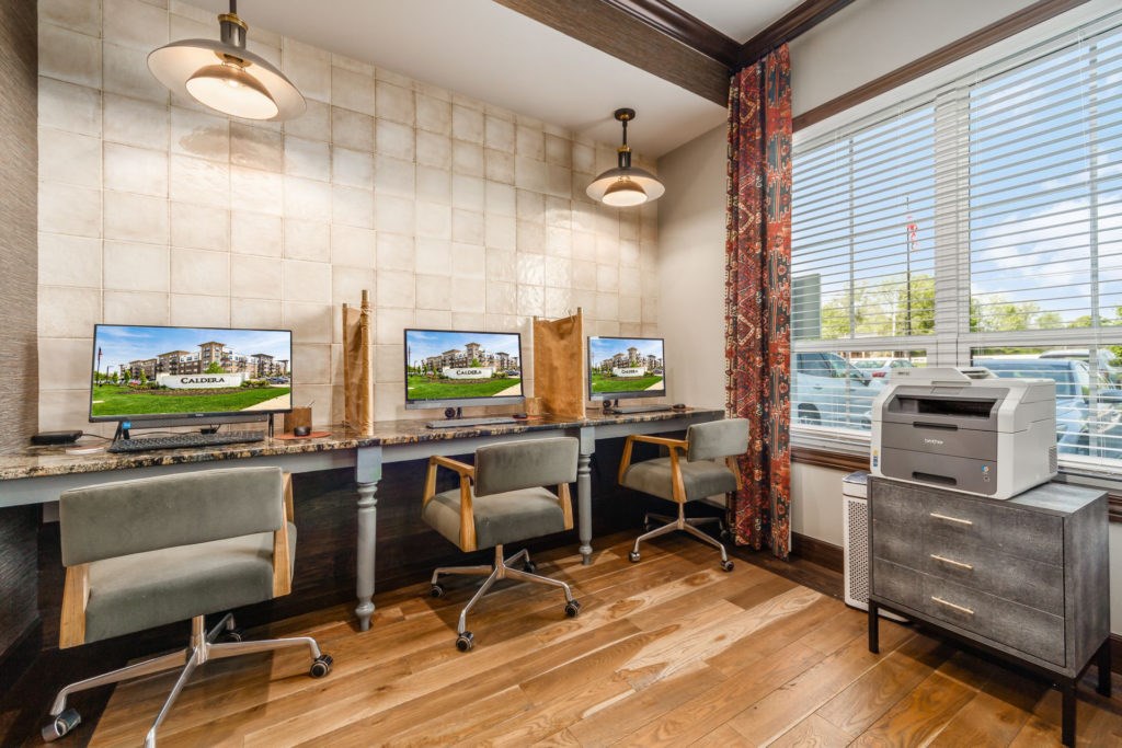 A room with a desk, chairs, and two computer monitors.