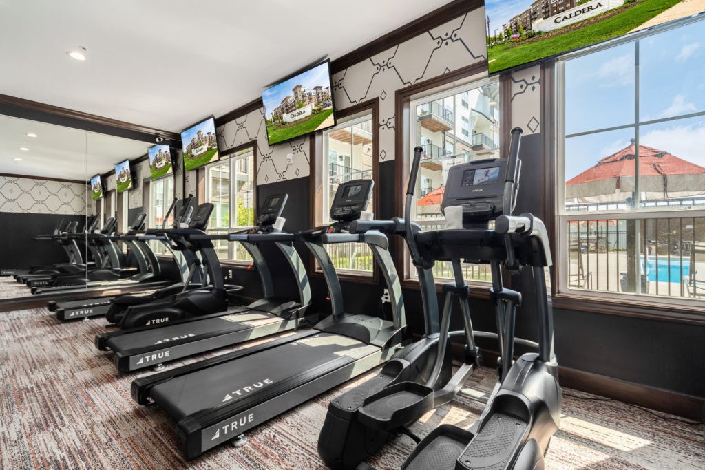 A gym with treadmills and a view of a pool and building outside.