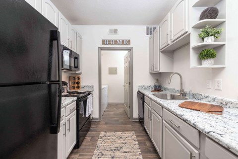 A kitchen with a black refrigerator and white cabinets.