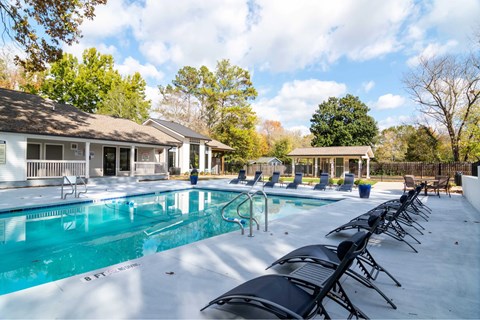 A pool with chairs around it and a building in the background.