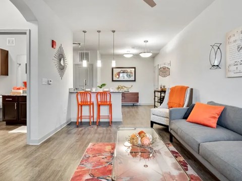 A living room with a grey couch, orange chairs, and a red rug.