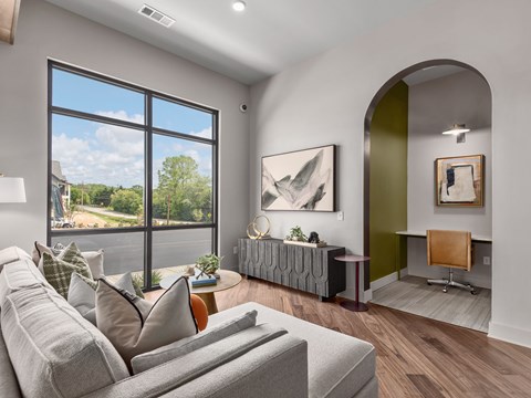 A modern living room with a grey sofa and a large window.