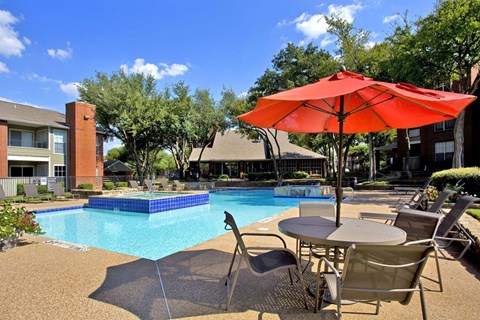 A red umbrella is on a patio table next to a pool.