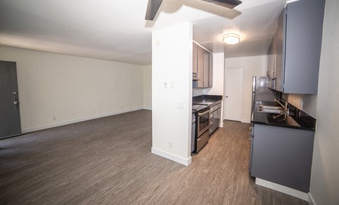 an empty living room and kitchen with a wood floor and black appliances