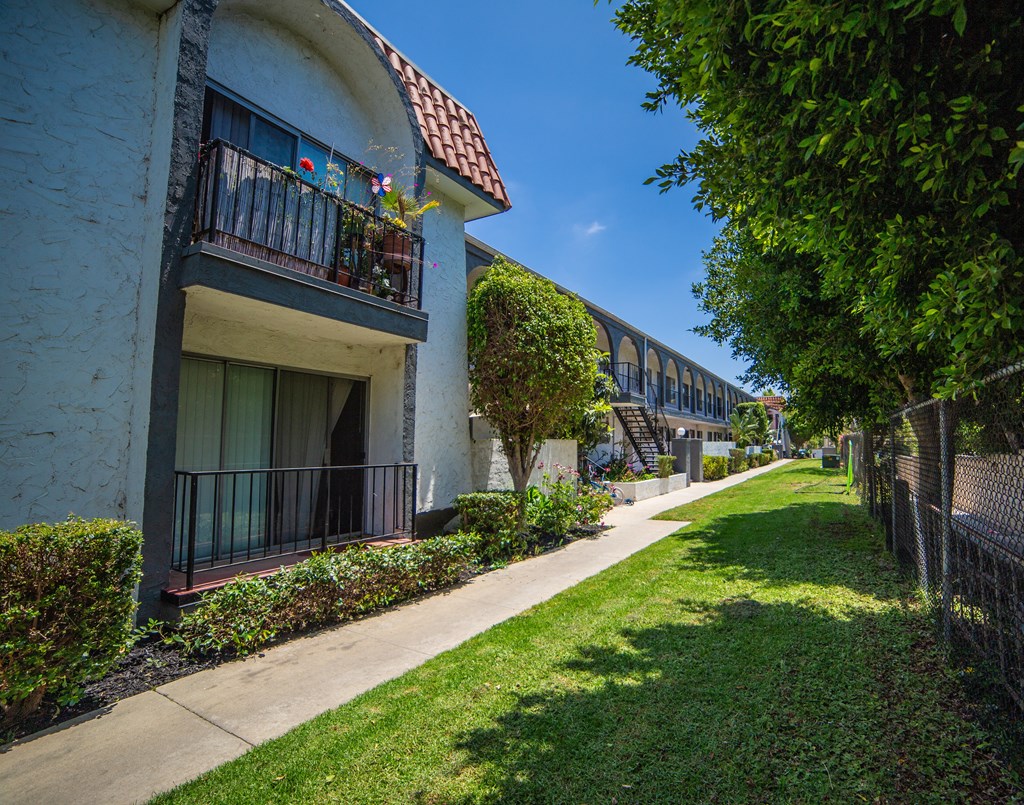 a sidewalk lined with plants and trees in front of building 182