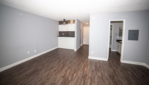 an empty living room with wood flooring and a kitchen