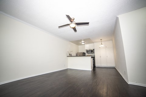an empty living room with a ceiling fan and a kitchen