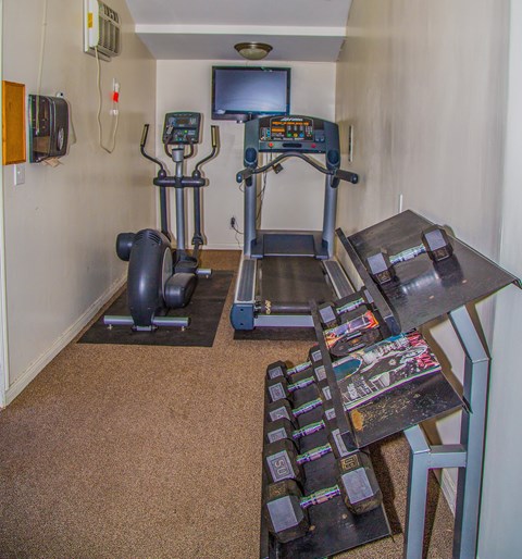 a room with a treadmill and a table with a television on the wall