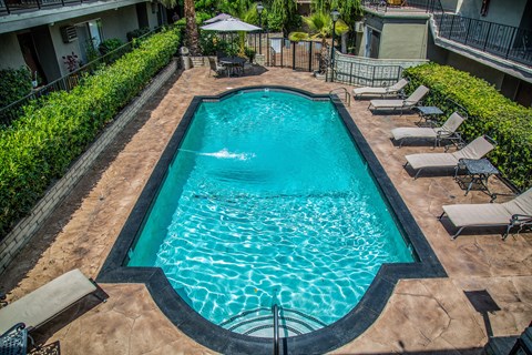 a swimming pool with lounge chairs and umbrellas in front of a building