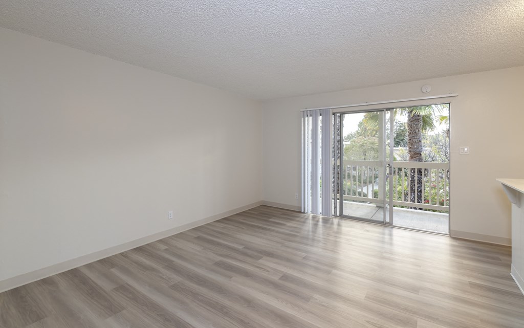 an empty living room with a sliding glass door to a balcony