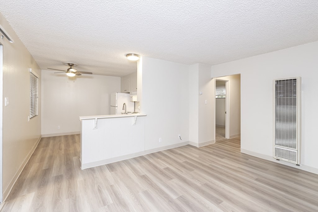 an empty living room with a kitchen and a ceiling fan