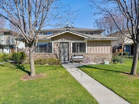 A house with a brown roof and a white fence is surrounded by a grassy lawn and trees.