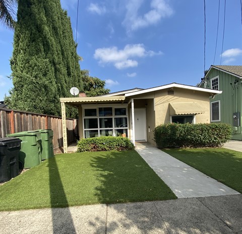 a small tan house with a driveway and a green fence