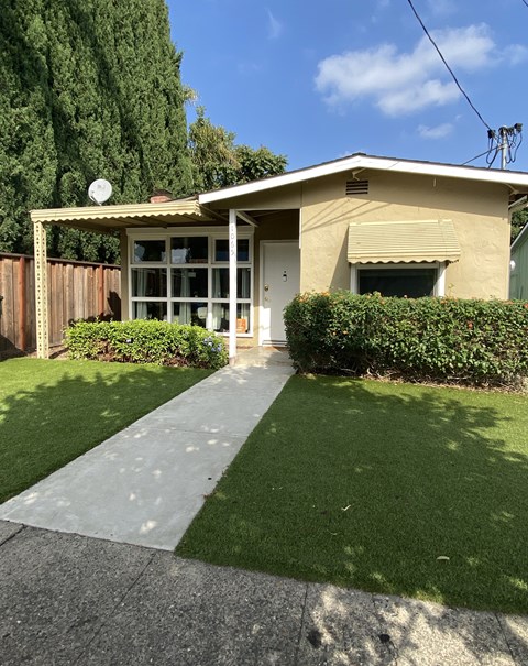a small tan house with a sidewalk and lawn