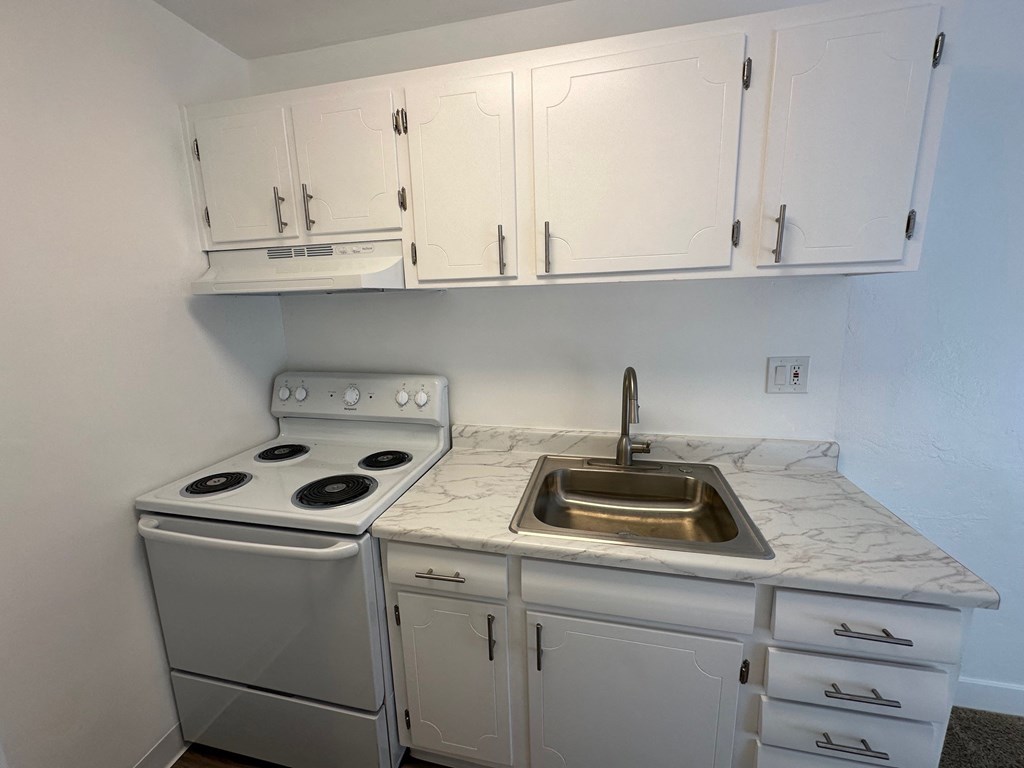 an empty kitchen with white cabinets and a stove and sink