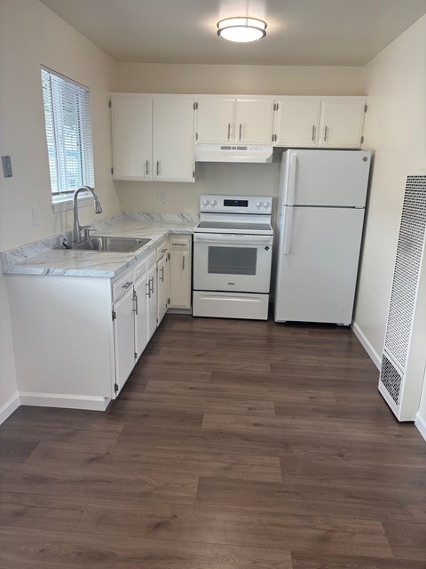 A kitchen with white appliances and wooden floors.