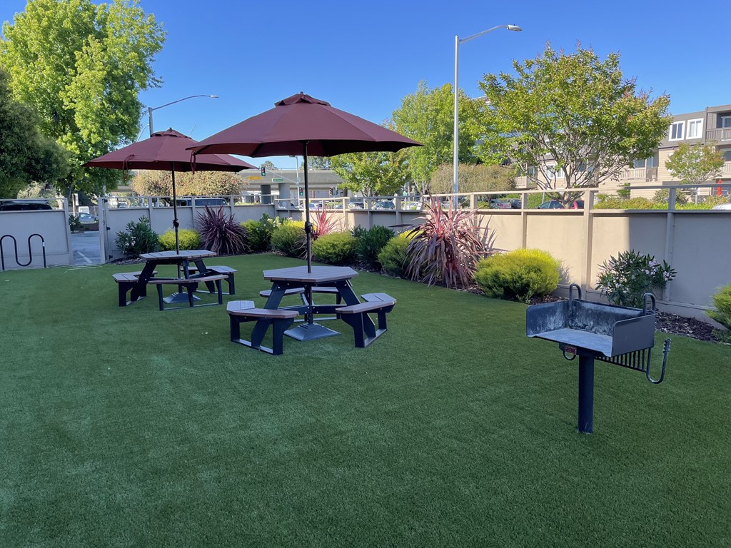 a patio with picnic tables and umbrellas and a grill