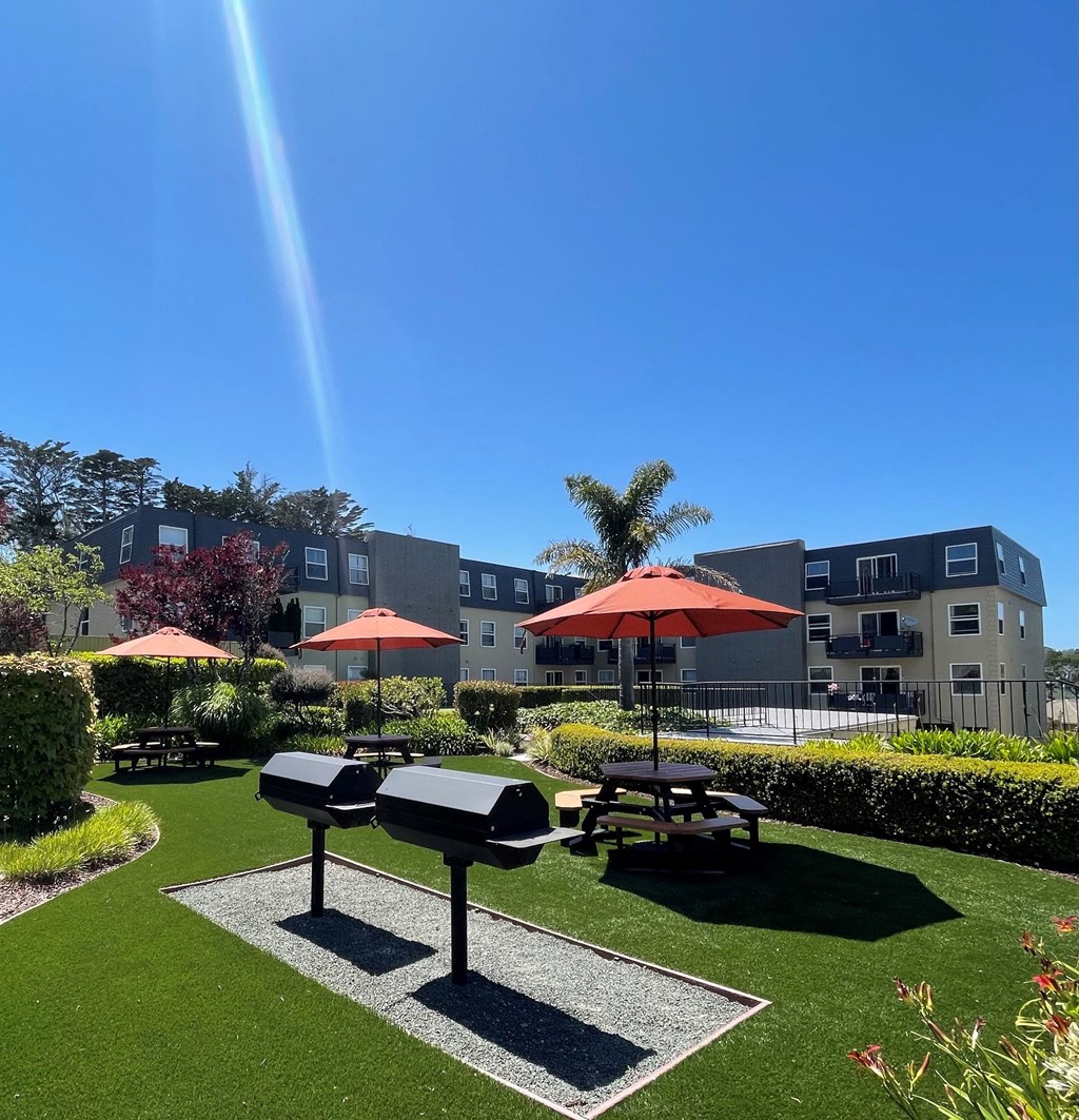 a park with picnic tables and umbrellas in front of an apartment building