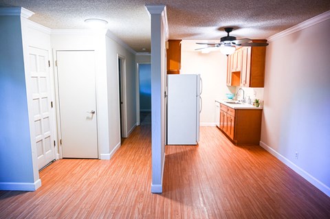 an empty living room with a kitchen and a ceiling fan