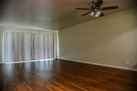 an empty living room with wood floors and a ceiling fan