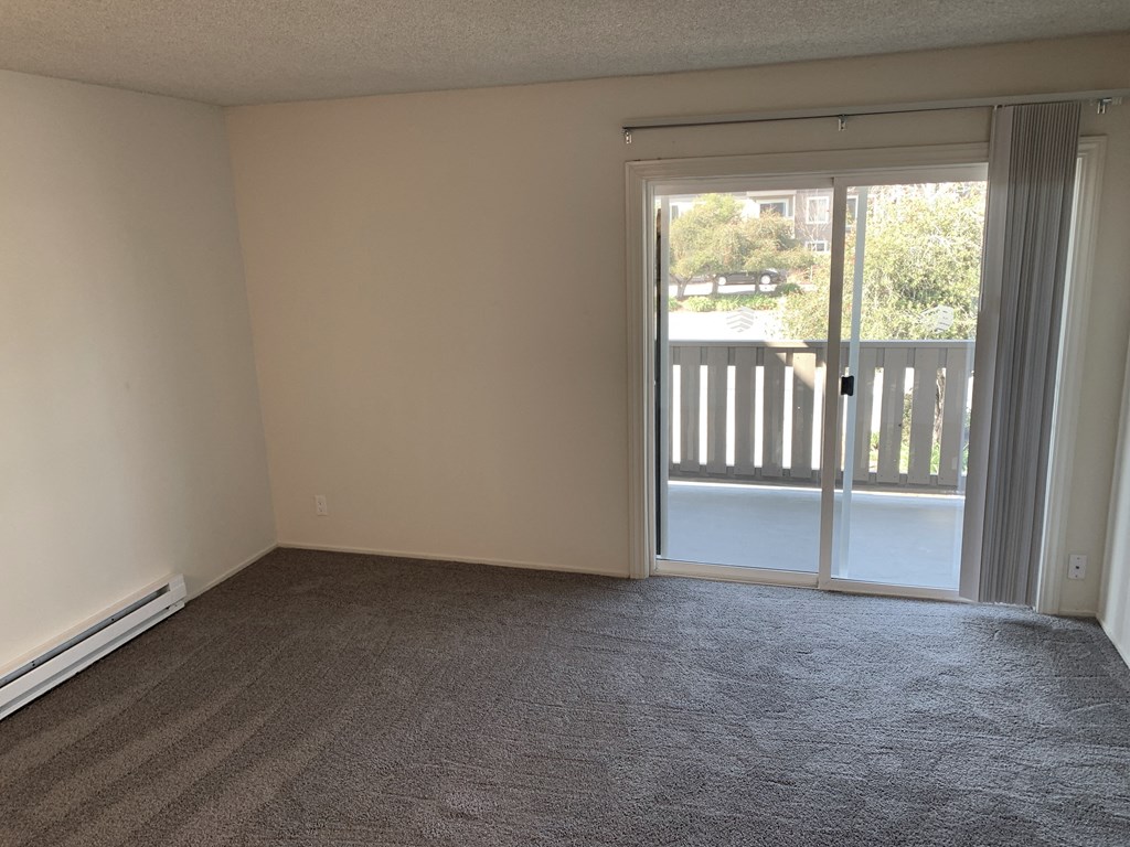 an empty living room with a sliding glass door to a balcony