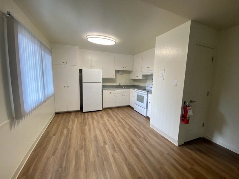 an empty kitchen with white appliances and wood floors