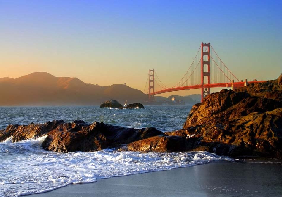 a view of the golden gate bridge over the water and rocks