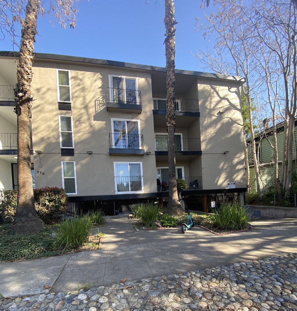 an apartment building with a sidewalk and trees in front of it