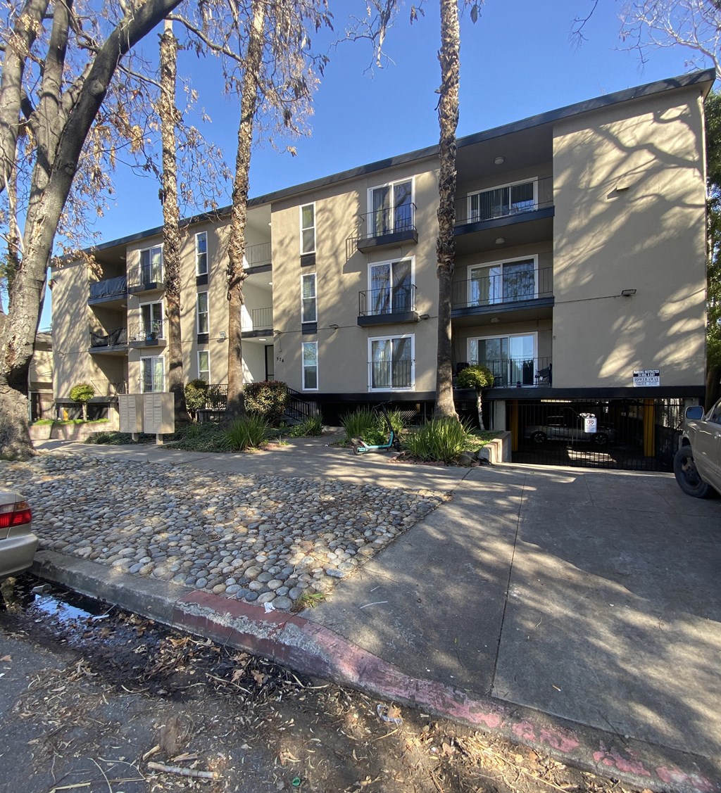 an apartment building with a gravel parking lot and trees
