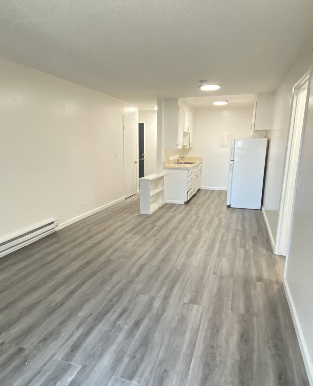an empty kitchen and living room with wood floors and a refrigerator