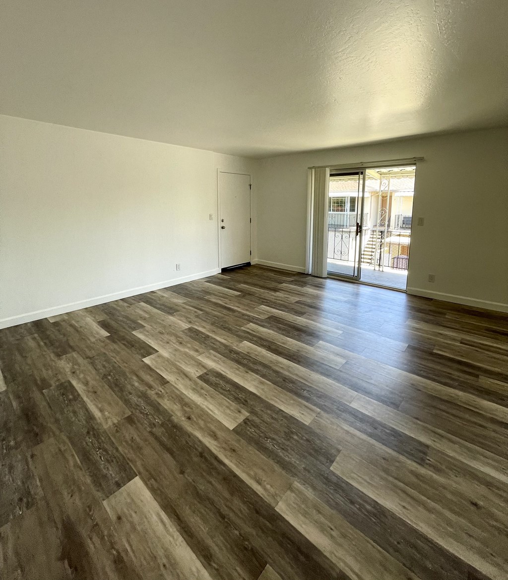 an empty living room with wooden floors and a door to a balcony