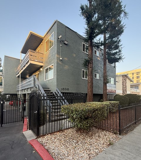 A grey building with a black fence and a red stripe on the sidewalk.