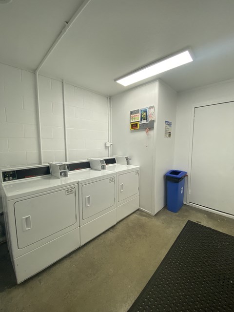 a room with four washing machines and a blue trash can