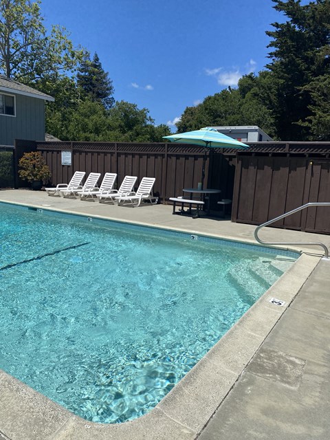 a swimming pool in a backyard with white chairs and an umbrella