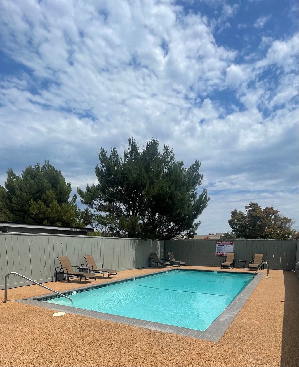 a swimming pool on a cloudy day in a backyard with chairs