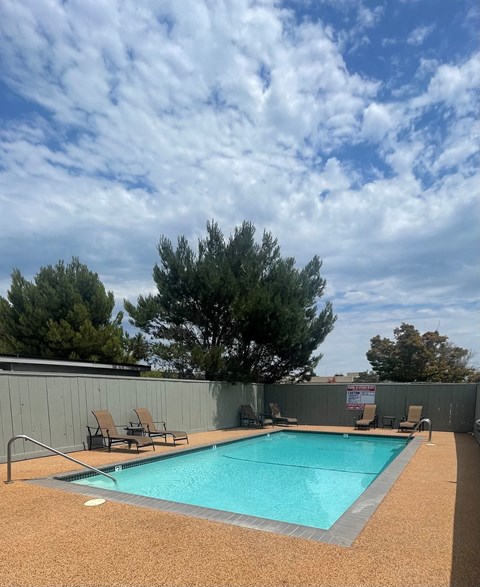 a swimming pool on a cloudy day in a backyard with chairs