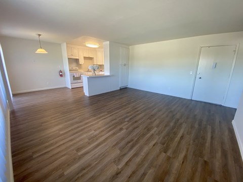an empty living room with wood flooring and a kitchen