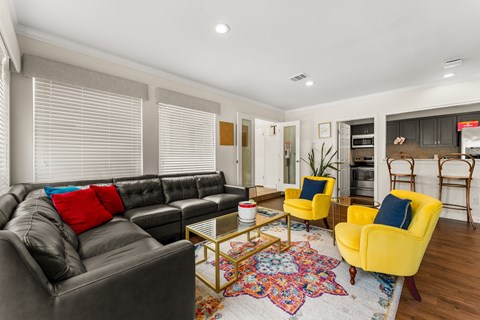 A living room with a black leather couch, yellow armchairs, and a colorful rug.