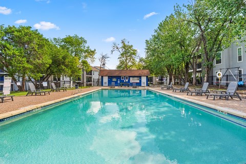 A swimming pool surrounded by trees and lounge chairs.