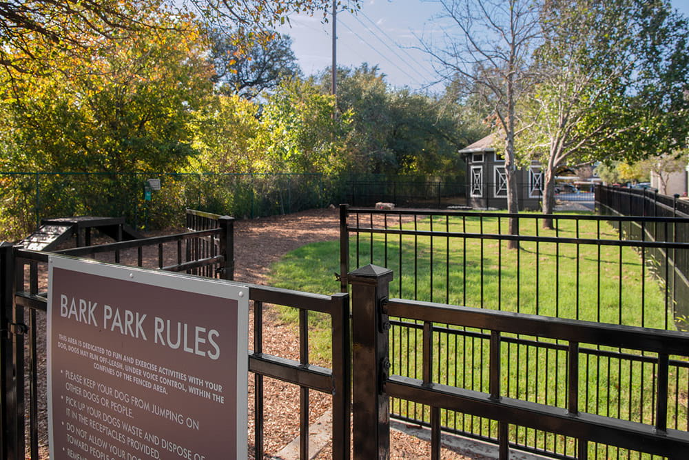 a sign for the bark park rules in front of a fence