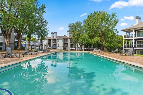 A swimming pool in a sunny day surrounded by chairs and trees.