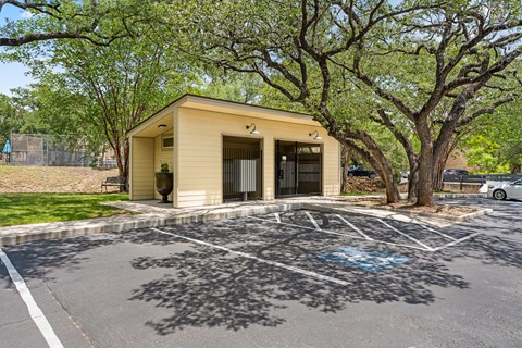 A small building with a yellow exterior is surrounded by trees and a parking lot with a blue graffiti design.
