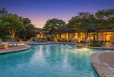 A beautifully lit pool area at dusk with a house in the background.