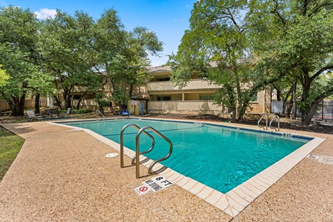 A pool surrounded by trees and a building in the background.