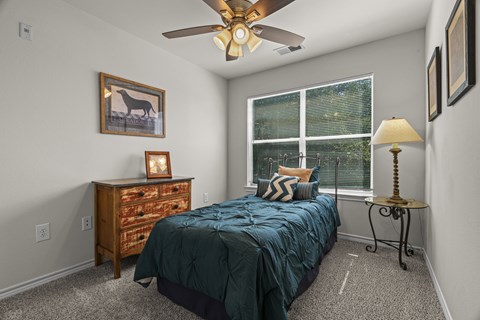 A bedroom with a bed, dresser, and a ceiling fan.