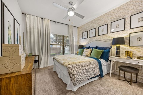 A bedroom with a bed, desk, and a ceiling fan.