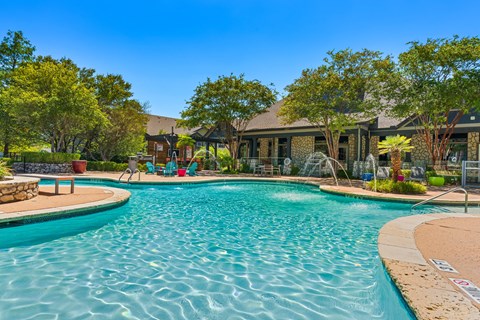 A large swimming pool surrounded by trees and a building in the background.
